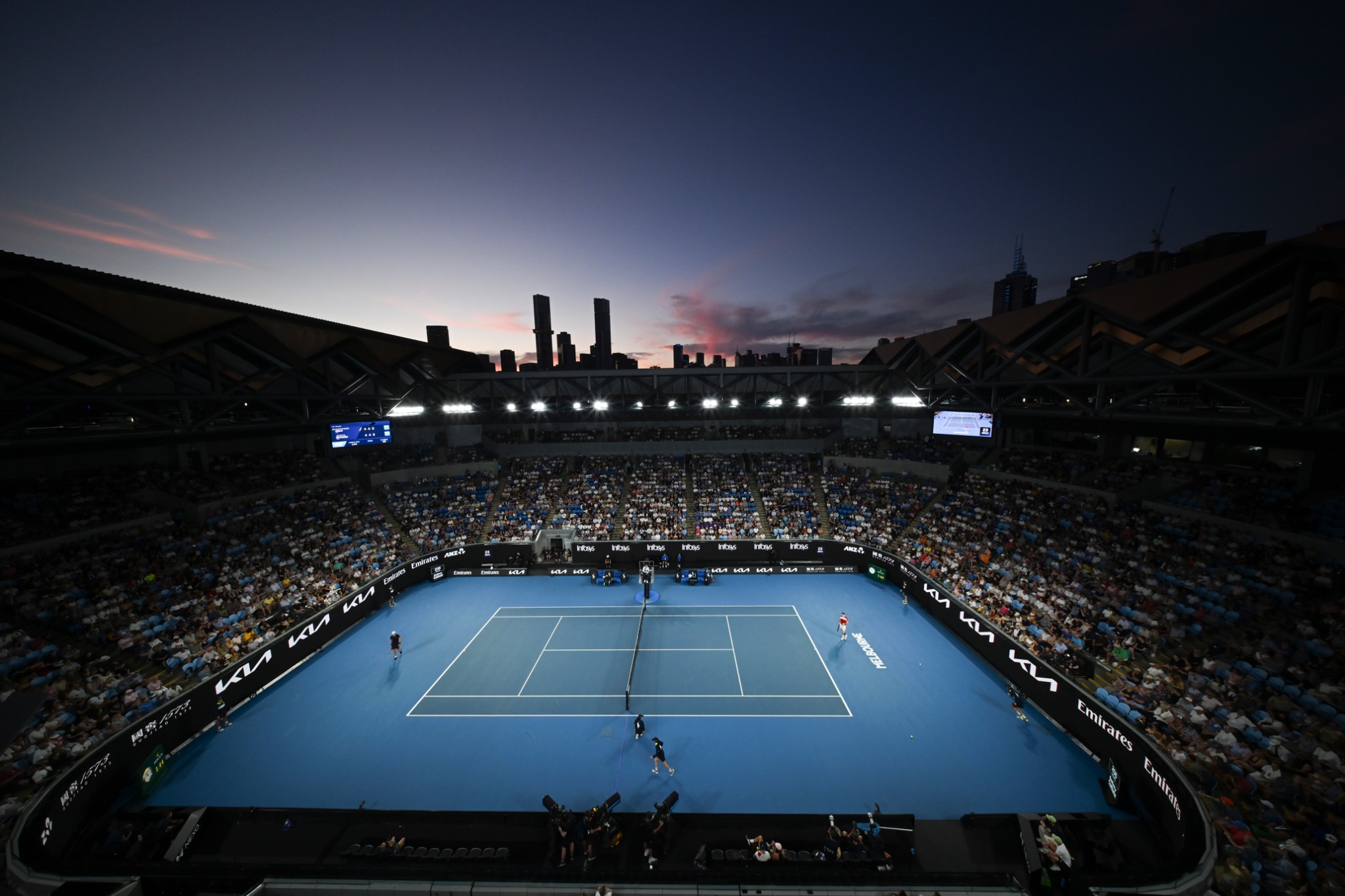 A packed Australian Open stadium at dusk with the blue court below